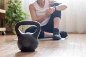 Mature woman sitting on a yoga mat, checking her fitness tracker after an authentic home workout, focusing on health, wellness, and a sustainable lifestyle, with a kettlebell in the foreground