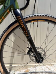 Batch GB.1 aluminum gravel fork with copper BATCH lettering, front quick-release hub, and disc rotor visible behind the tan-wall tire.